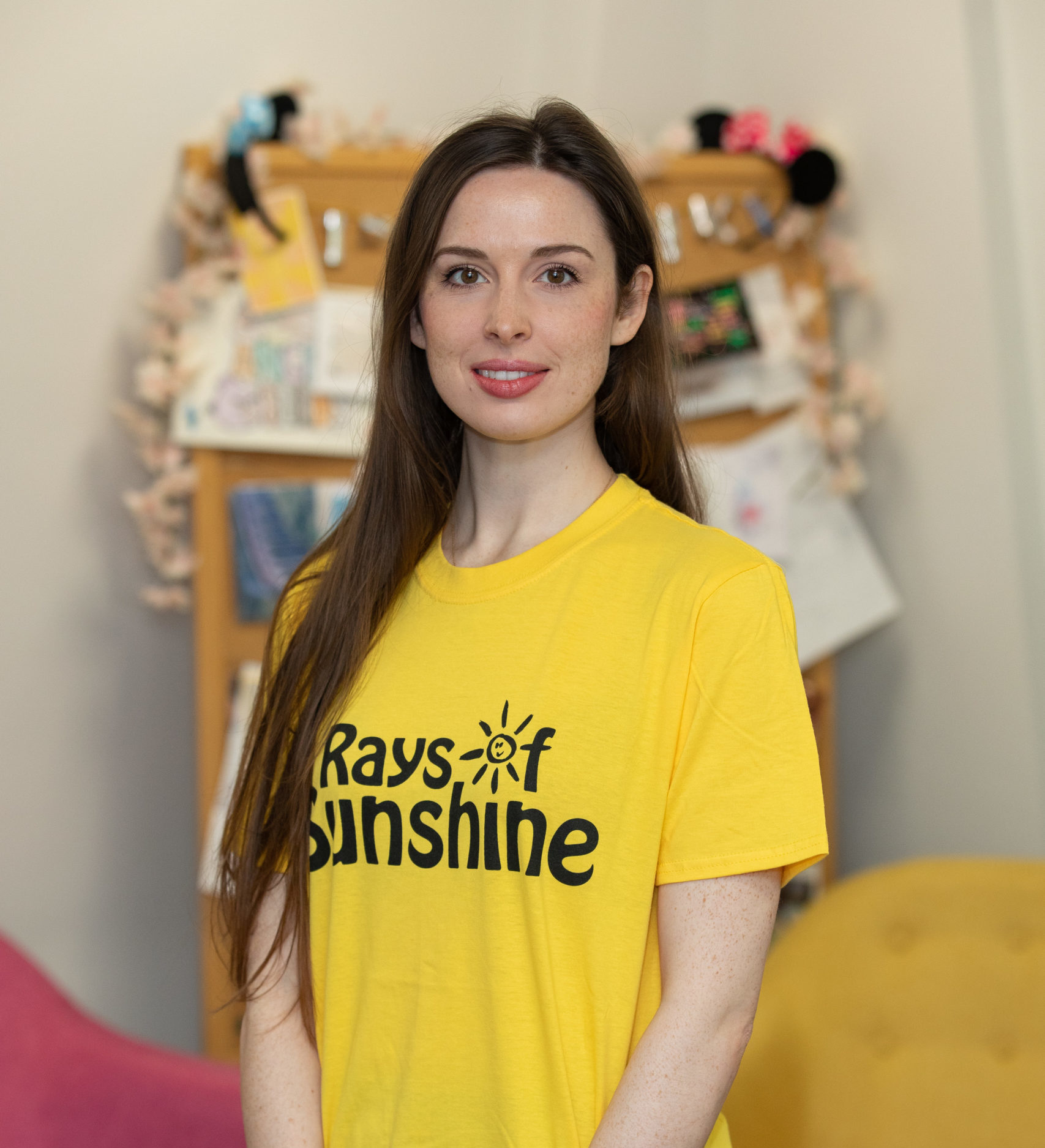 Sophie is wearing a Rays of Sunshine t-shirt. She is standing and has brown hair.