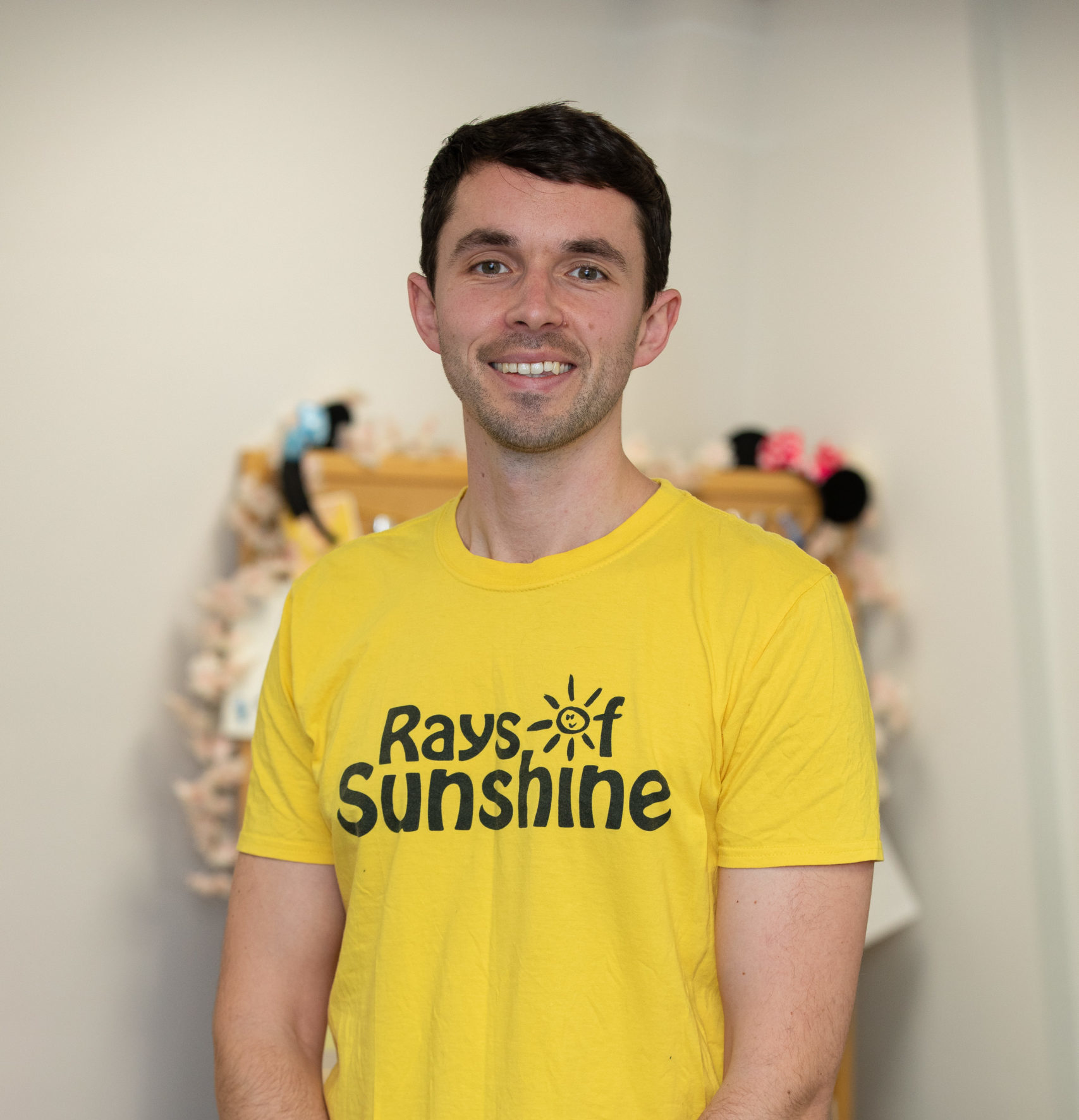 Jack is standing and is wearing a Rays of Sunshine t-shirt. He has dark hair.