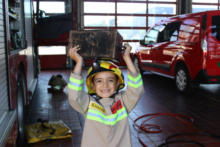 Small boy in a firefighter uniform holding a chest above his head.