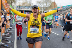 Runner in yellow vest, celebrating as she runs the London Marathon