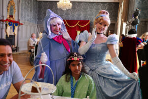 Little girl in green dress poses with The Fairy Godmother and Cinderella
