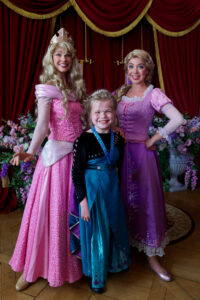 Princess Aurora and Rapunzel pose with little girl wearing blue/green dress