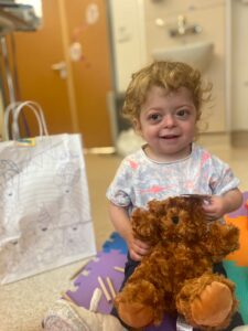 Little girl sits on the hospital floor, while holding a teddy bear
