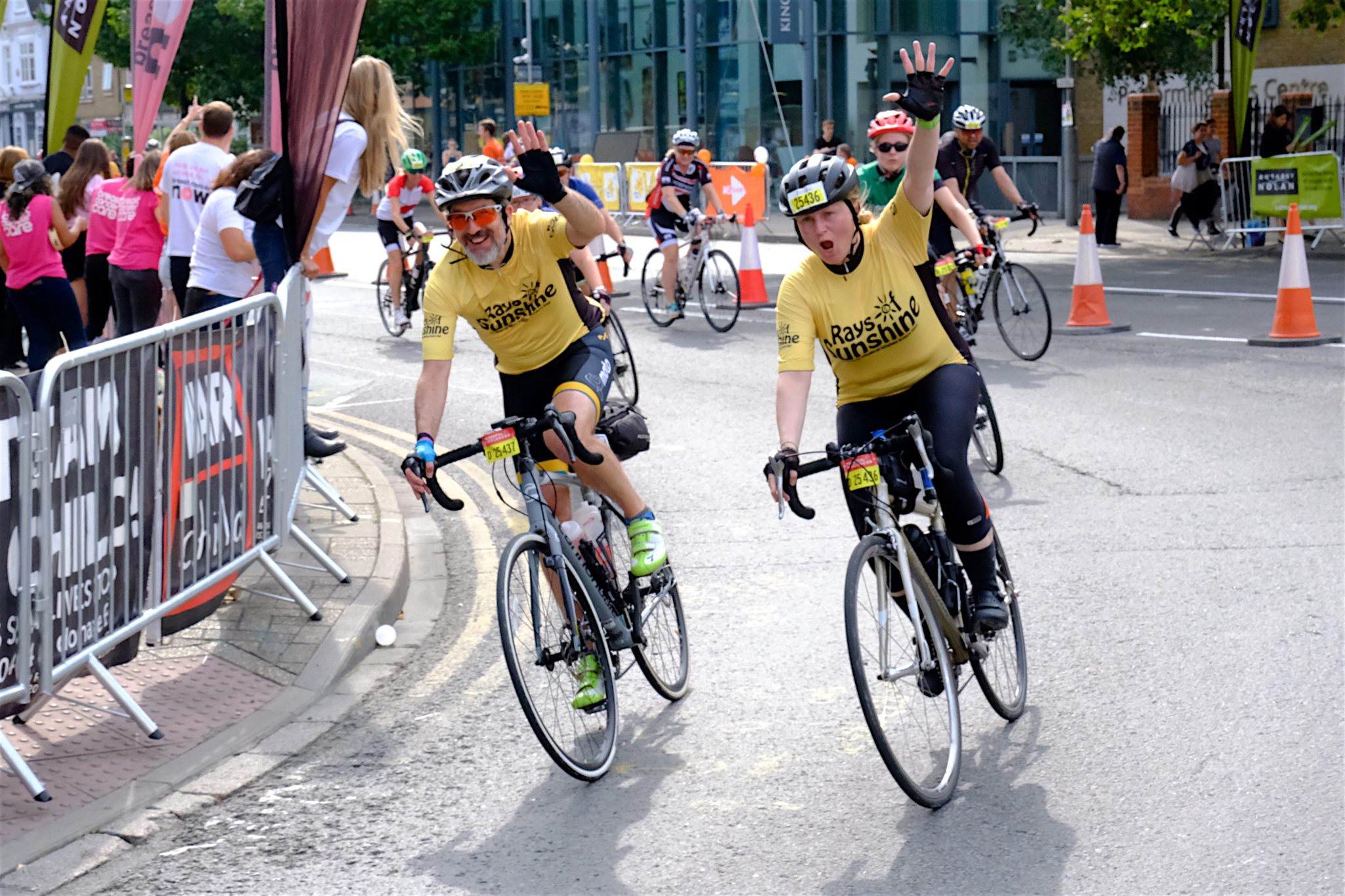 Two cyclists cycling with Rays of Sunshine t-shirts on