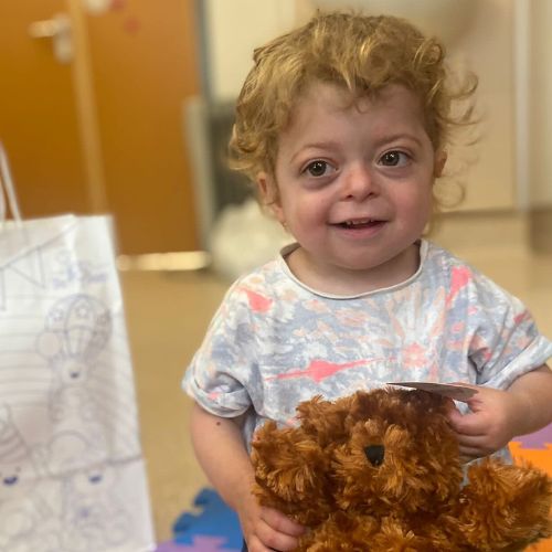 Little child sits on the hospital floor, while holding a teddy bear