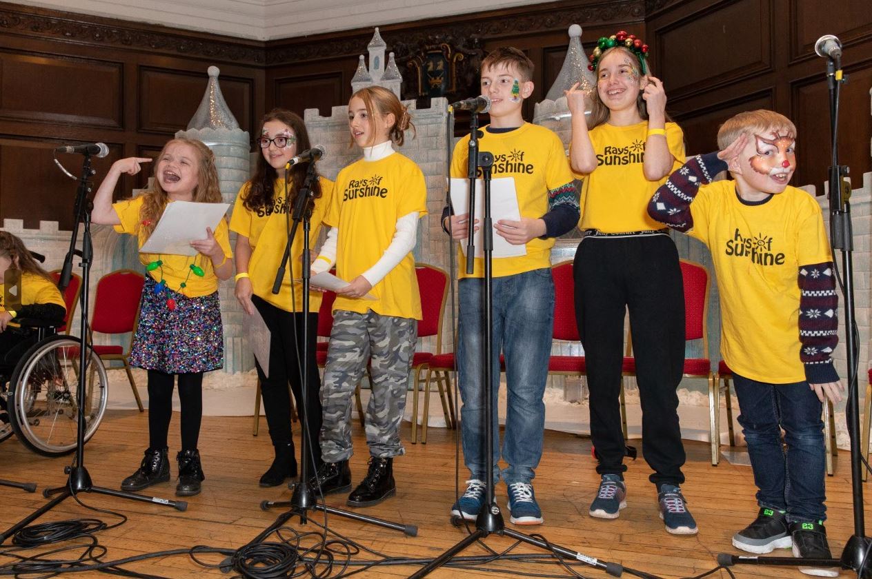 Group of young children in all wearing yellow Rays of Sunshine t-shirts singing into microphones