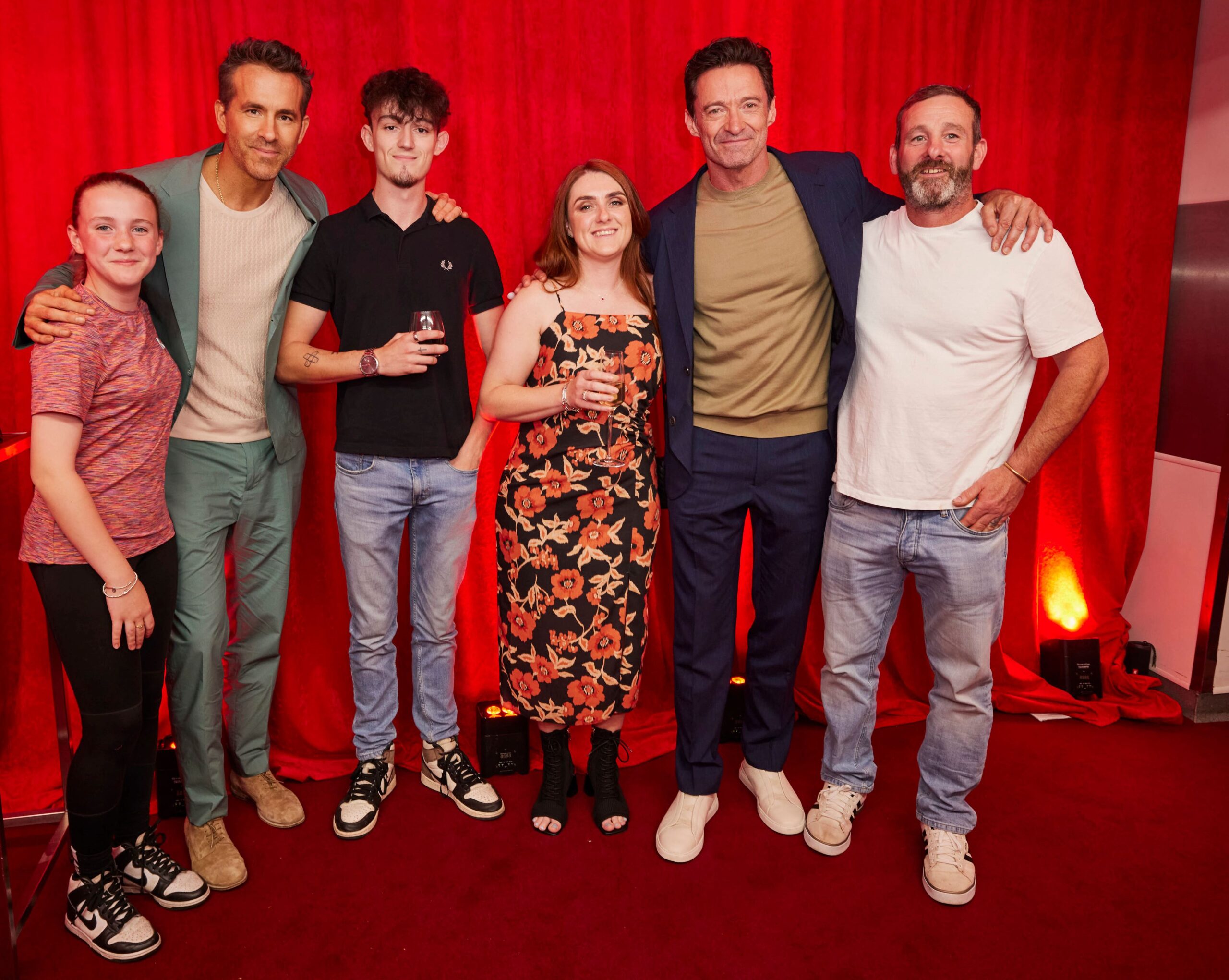 Group picture of six people in front of a bright red curtain. There are four men and two women, all in more casual clothing.