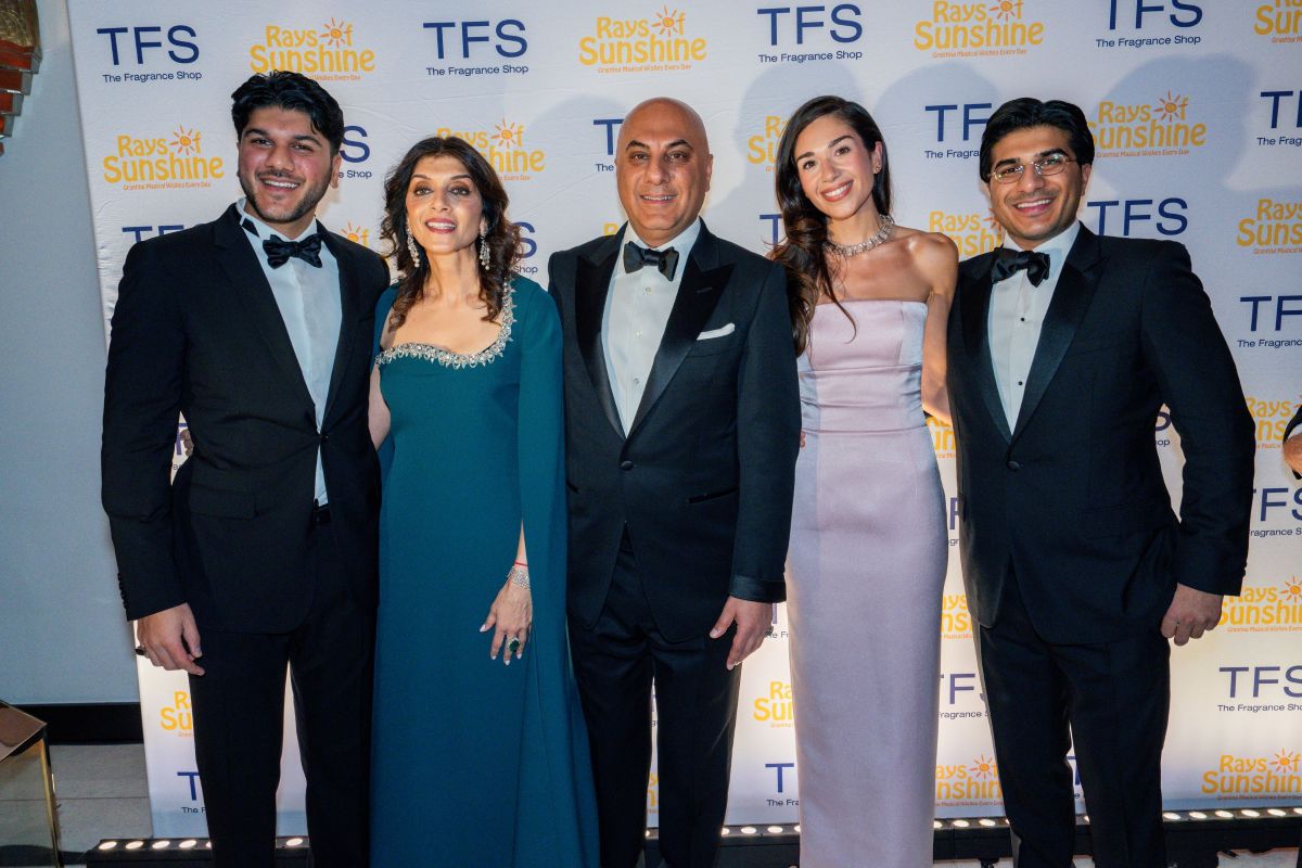 Group of people in black tie outfits smile for a group pic in front of a step and repeat board