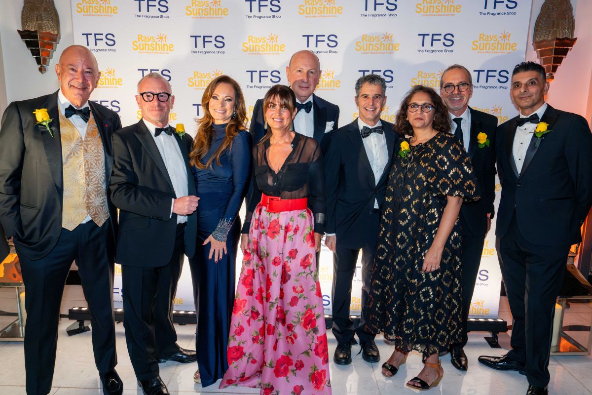 Group of people in black tie outfits smile for a group pic in front of a step and repeat board