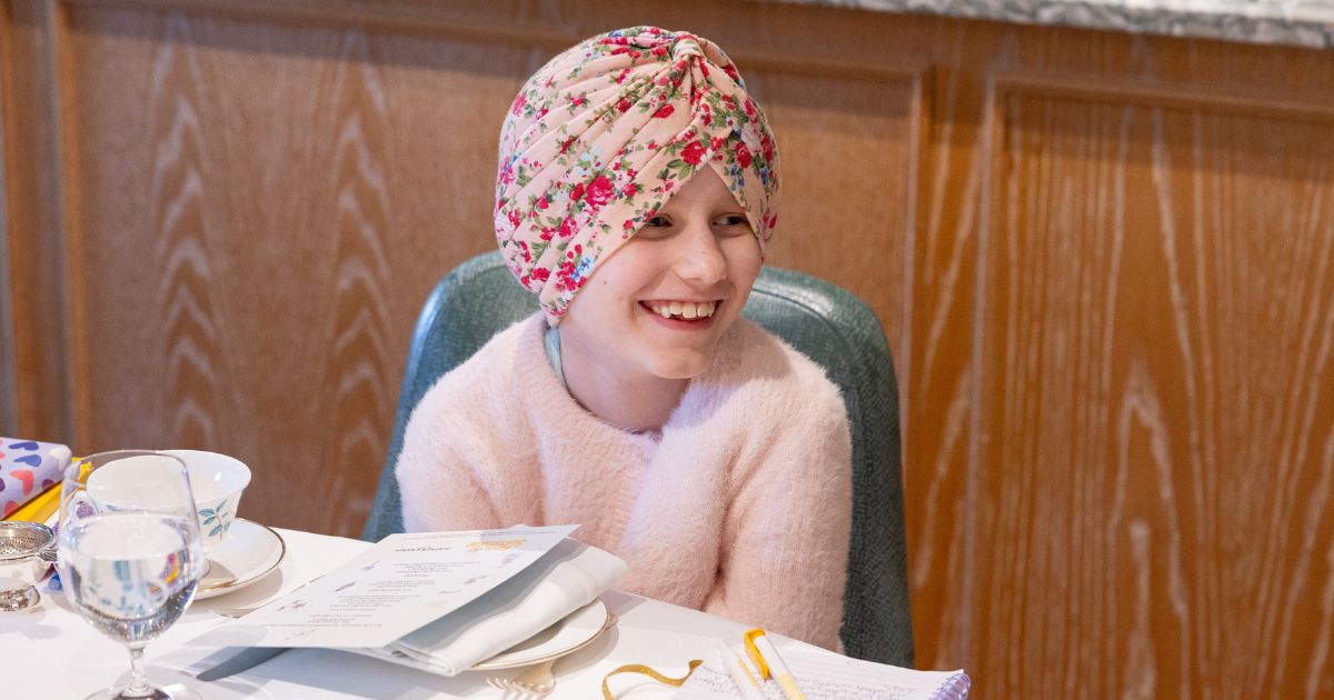 A girl smiling at the camera wearing a flowery headcover sat a table