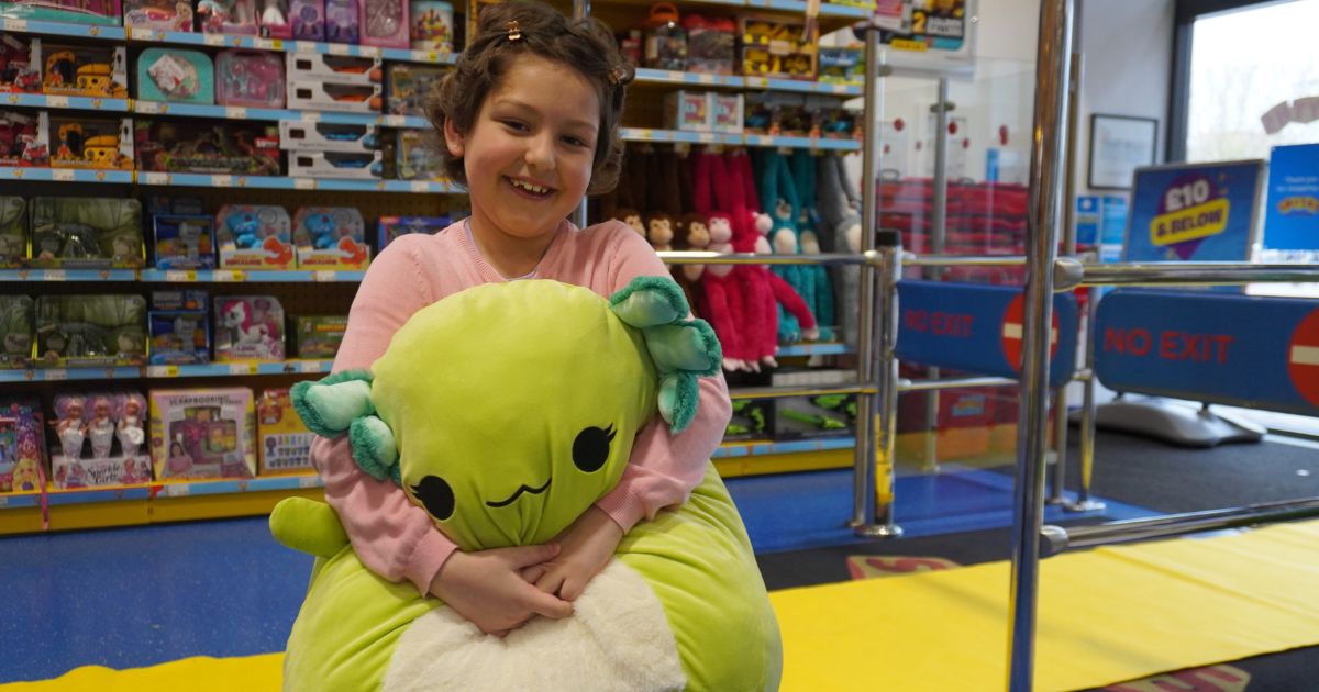 A girl holding a stuffed animal in a toystore smiling