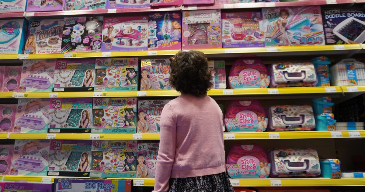 A young girl in a pink jumper looking at a shelves full of toys