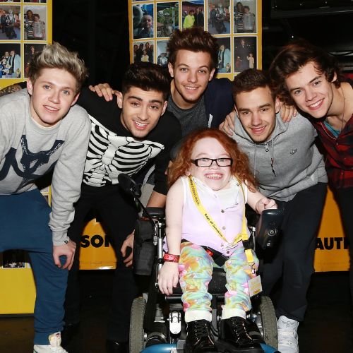 One direction band members smiling at the camera with a young person in a wheelchair