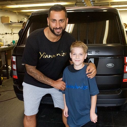 Yiannimize smiling to camera with a small boy in front of big car