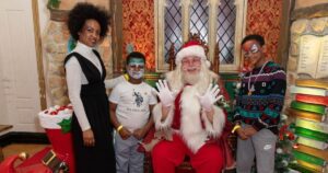 Santa in his grotto with two smiling children and their mum all with facepaint on