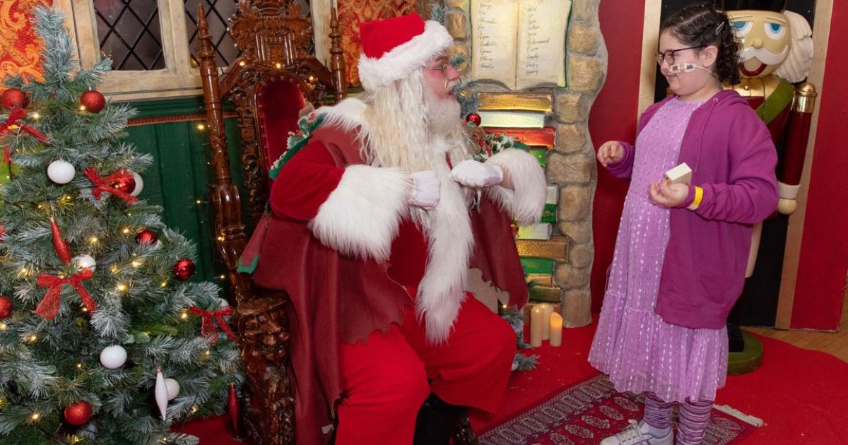 Santa in his grotto with a young girl they are smiling at each other