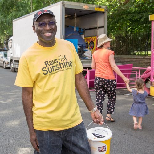 Volunteer wearing a yellow Rays of Sunshine t-shirt smiling to camera and holding a fundraising bucket