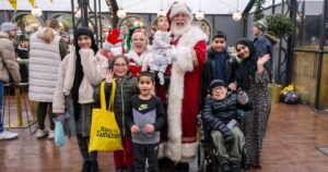 A family posing for a photo with Santa and Mrs Claus smiling and waving to camera