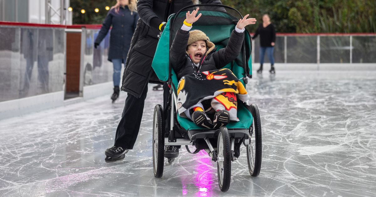 A child in a stroller on an ice rink with their hands in the air