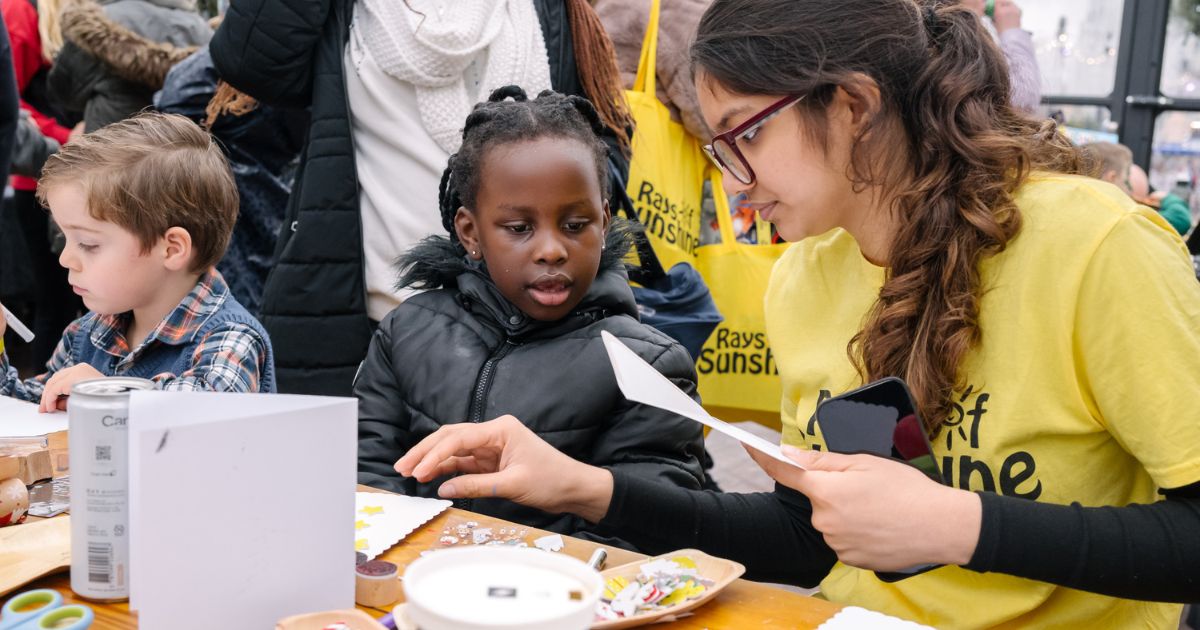 A Rays of Sunshine volunteer and a child at an arts and crafts table