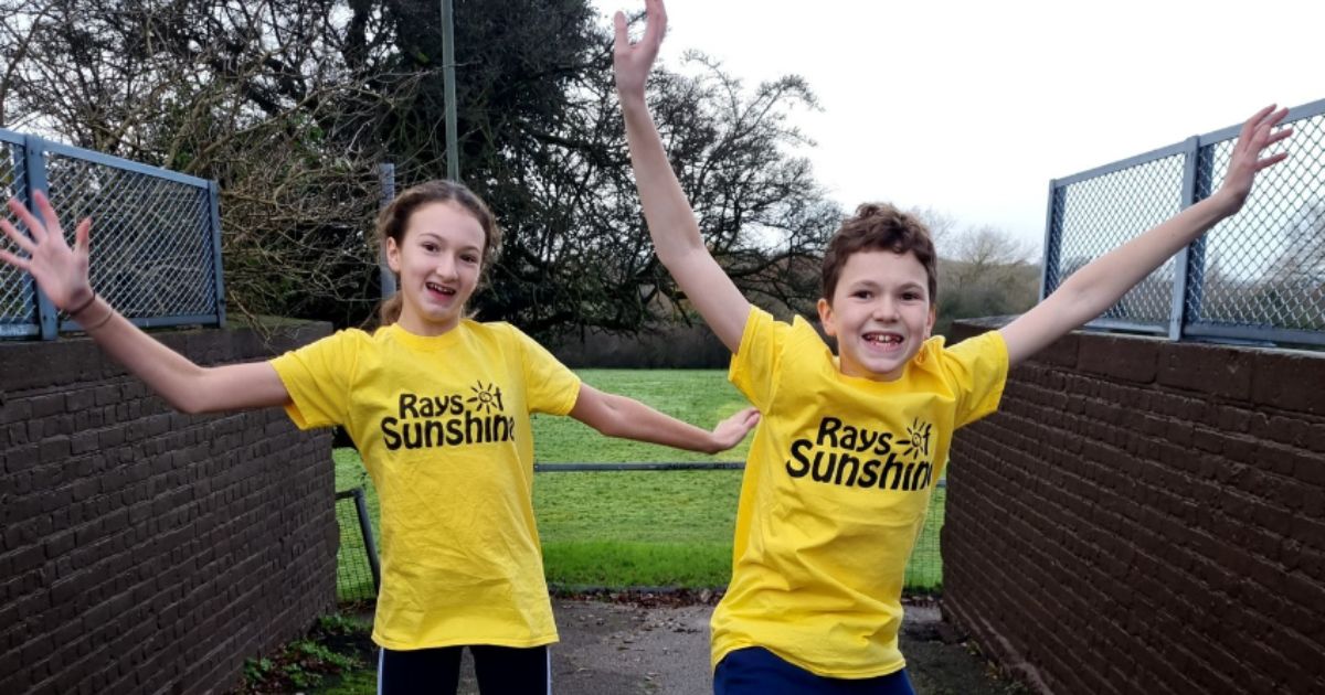 A couple of kids in yellow Rays of Sunshine t-shirts jumping in the air with their arms up