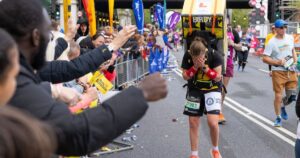 A person with a fridge on their back running the London Marathon looking overwhelmed by the crowd's support