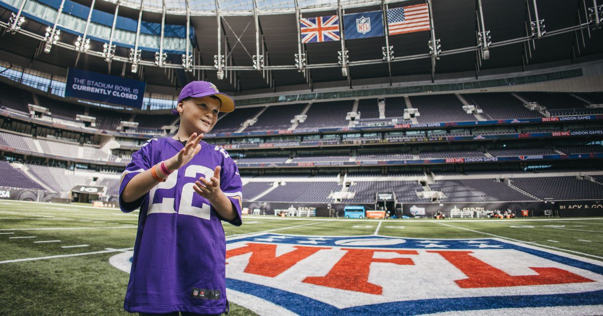 A child in a purple american football jersey in a stadium clapping his hands