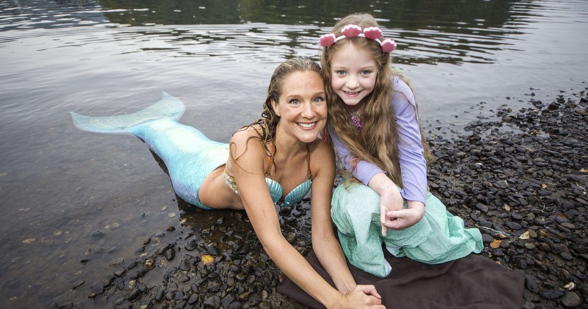 A woman dressed as a mermaid posing for a photo with a girl in a mermaid garment