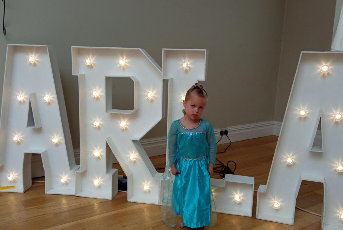 Little girl in blue princess dress smiles for the camera in front of big free standing letters that say ARLA