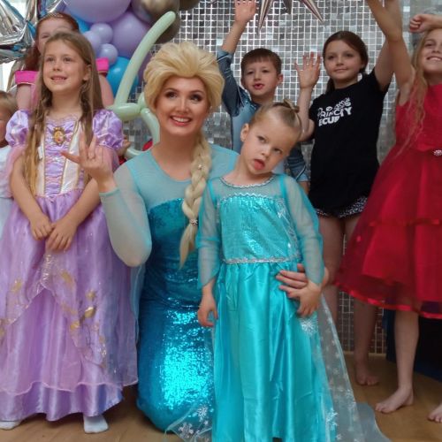 Little girl poses for a pic while dressed in a blue princess dress. She stands with a woman who is dressed at Disney princess Elsa