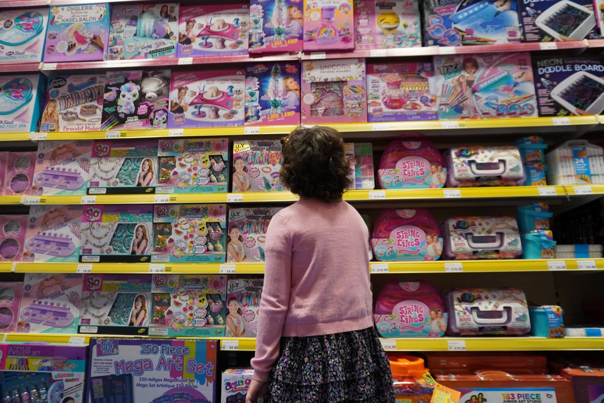 Little girl gazes up while stood in the aisle of a toy shop. Her back is to the camera