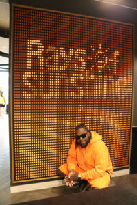 Man in orange tracksuit crouches in front of a feature wall that says Rays of Sunshine