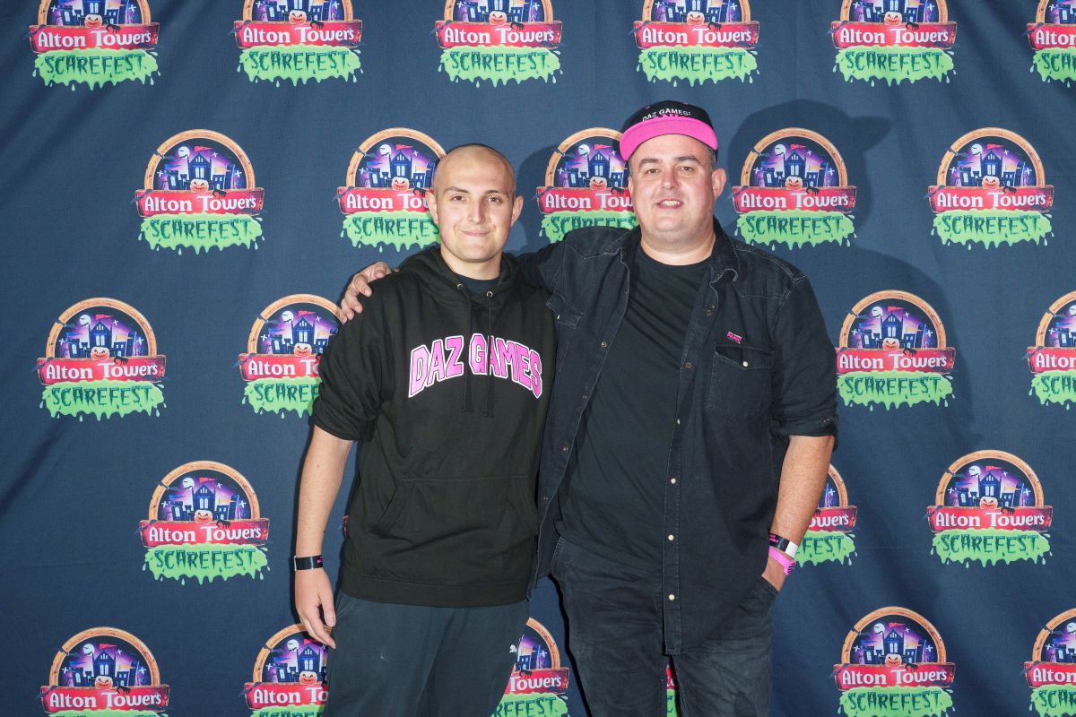 Two people stand while hugging each other. They are stood in front of a press board featuring the Alton Towers logo.