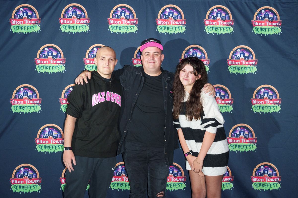 Three people stand while hugging each other. They are stood in front of a press board featuring the Alton Towers logo.