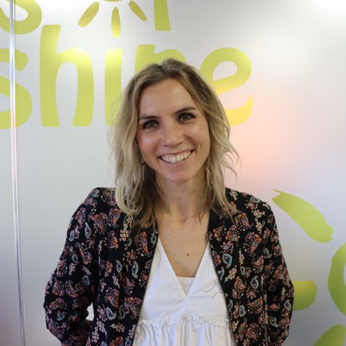 Woman smiles for the camera - she wears a white top and patterned jacket