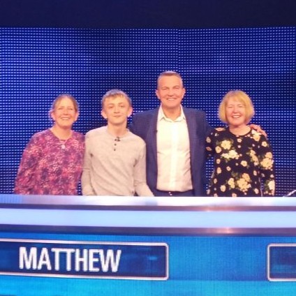 Four people stand together for a picture on the set of a gameshow. One is a teen boy