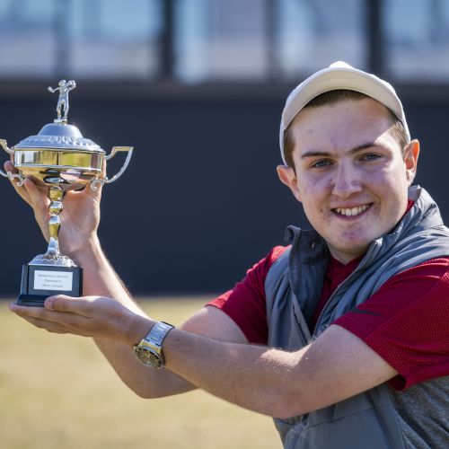 Teen boy in golfing outfit and cap holds a trophy aloft