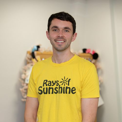 Jack is standing and is wearing a Rays of Sunshine t-shirt. He has dark hair.