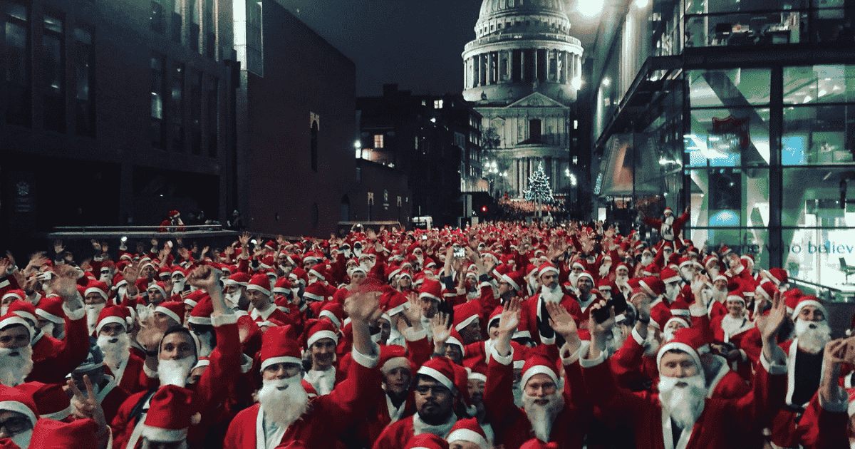 A mob of people dressed up as Santa running down a street in a city
