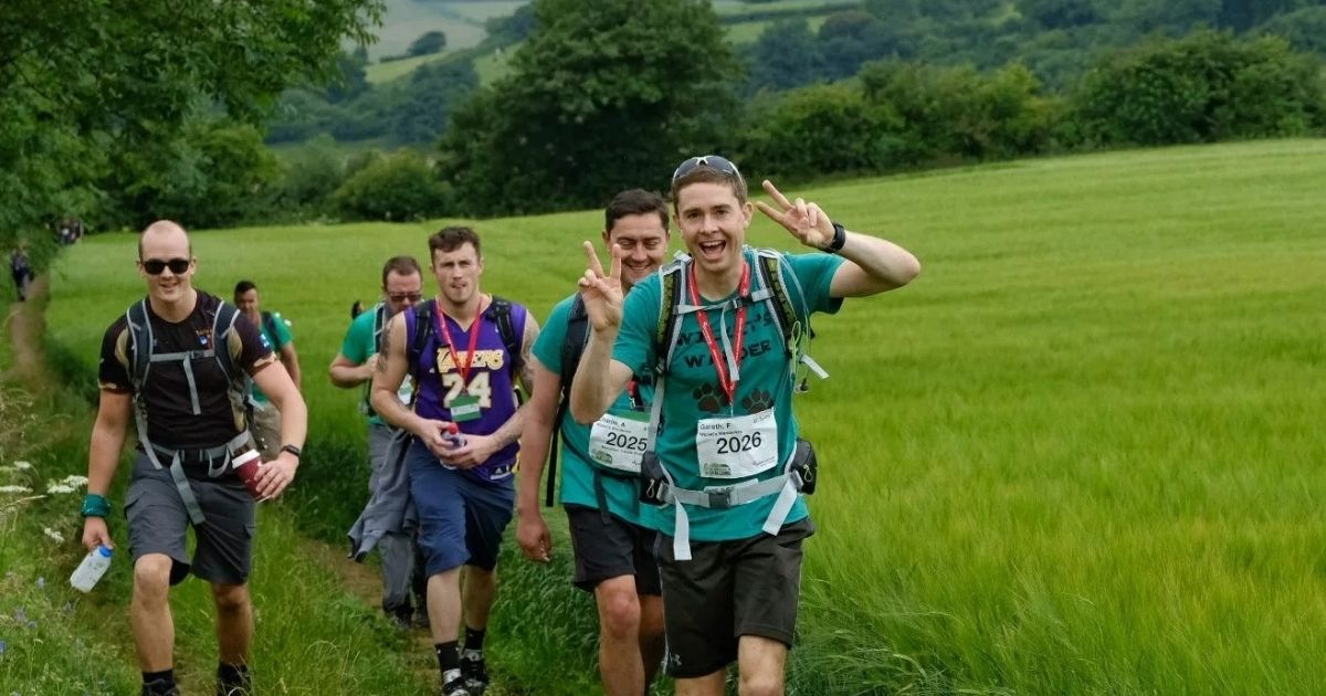 Group of guys hiking with a green scenic background with one throwing up a peace sign