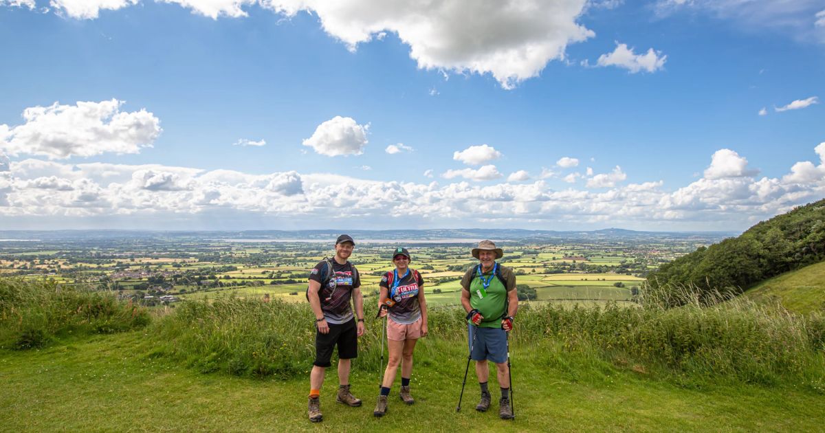 3 people standing on top of a hill with sky and clouds in background