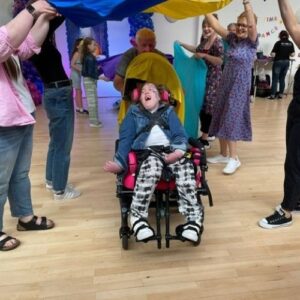 Teen girl in a wheelchair smiling and being pushed under colourful sheets at a party