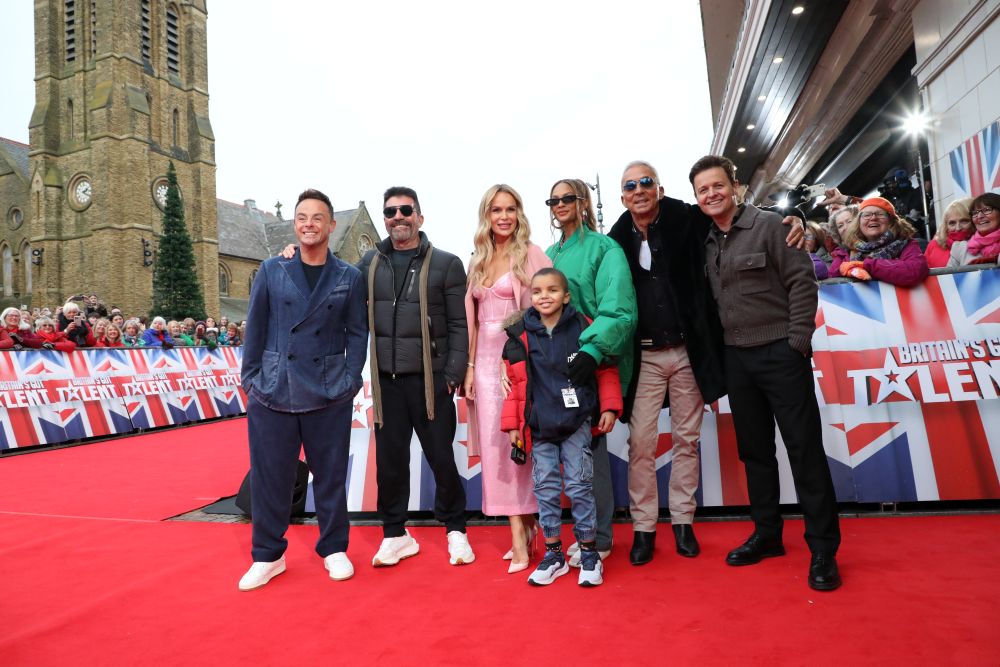 Little boy stands on a red carpet with all the judges of Britain's Got Talent