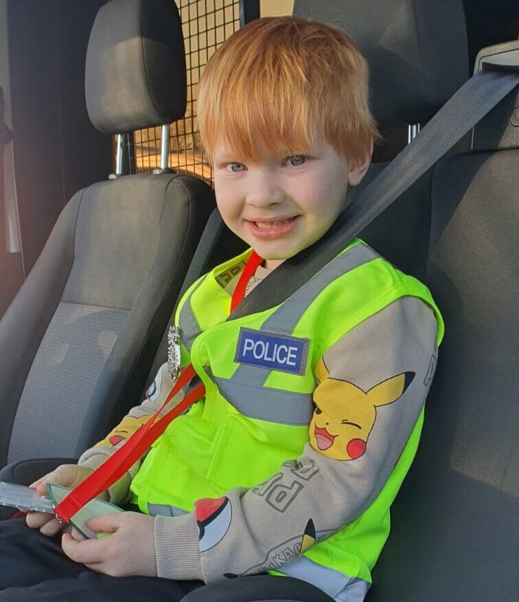 Little boy sat in a police car while wearing a high vis jacket