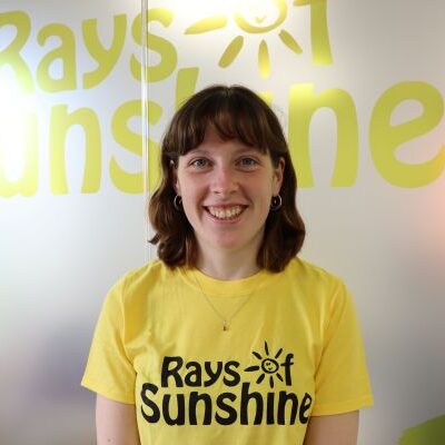 Woman with brown hair and wearing a yellow t-shirt smiles at the camera
