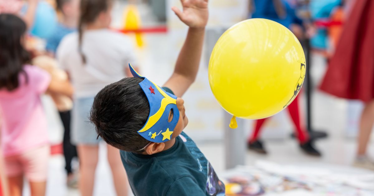 Boy with superhero mask plays with yellow balloon