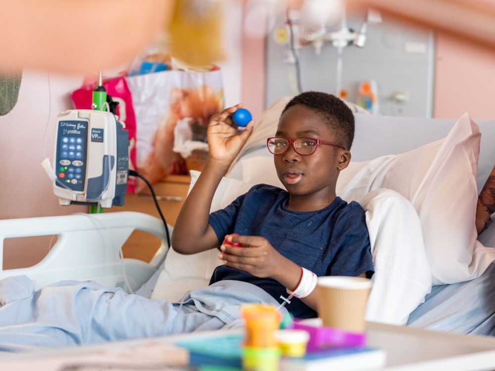 Little boy plays for a maraca while laying in a hospital bed
