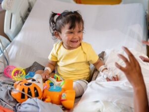 Little girl smiling while sat in a hospital bed with lots of toys around her
