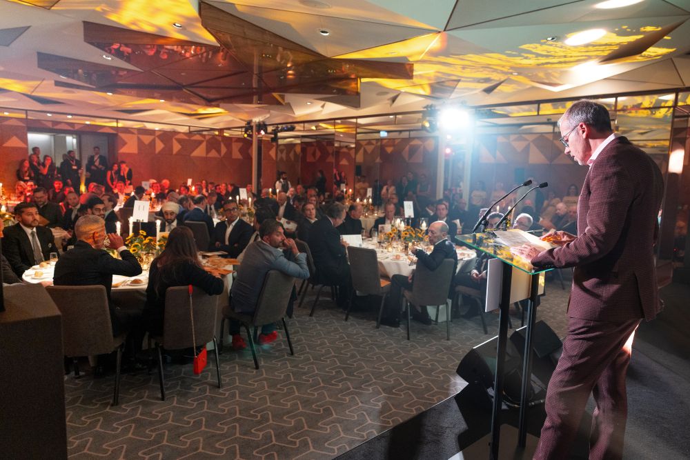 Full banquet hall of dinner guests watch as man delivers speech