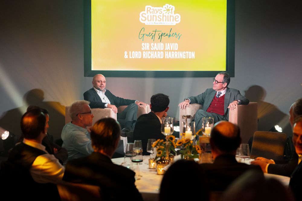 Two men sit on stage in front of dinner guests